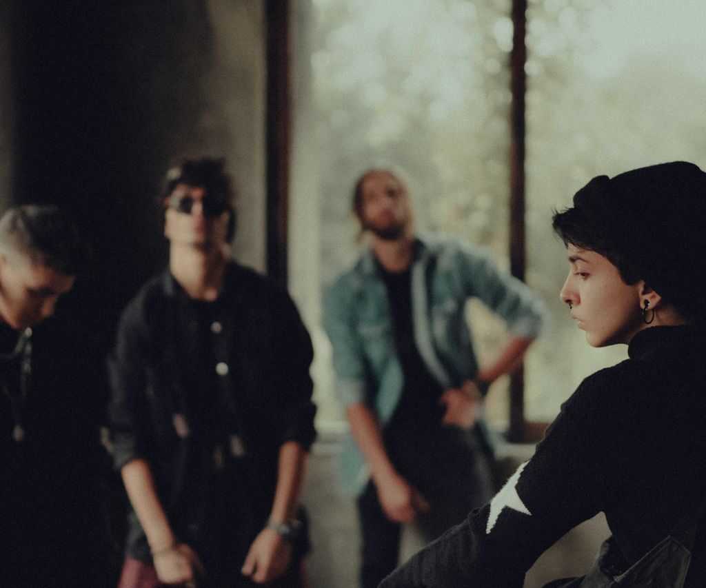 A fashionable group of young adults poses in a dimly lit room, evoking a sense of mystery.